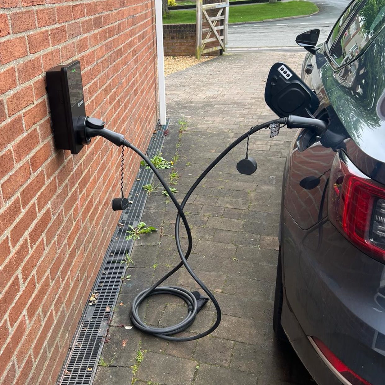 Wall-mounted smart EV charger on a house wall with an electric car charging